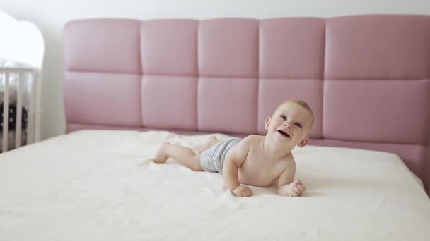 Bebé sorrindo, bebê bonito deitado na barriga na cama dos pais — Vídeo de Stock