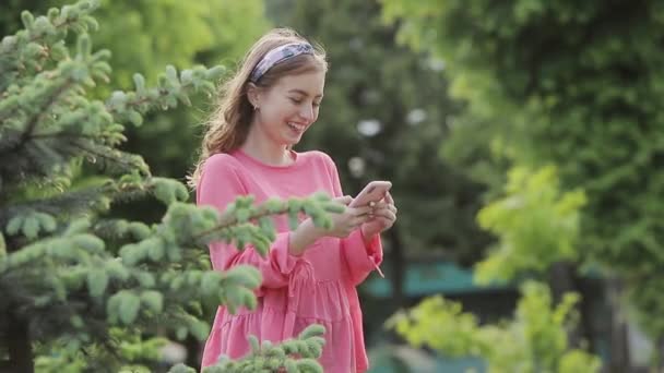 Menina bonita com encantador sorriso andando no parque e usando telefone móvel . — Vídeo de Stock