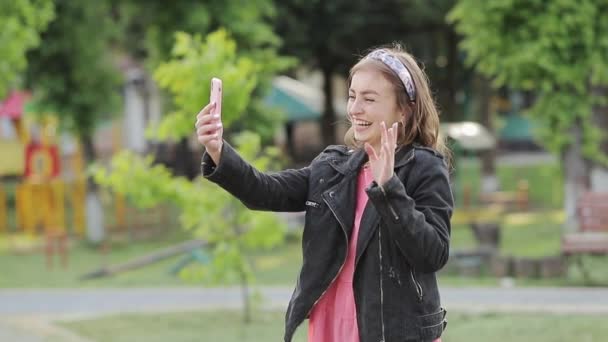 Belle jeune fille aux cheveux bouclés foncés à l'aide de son téléphone portable, en plein air. La blogueuse diffuse . — Video