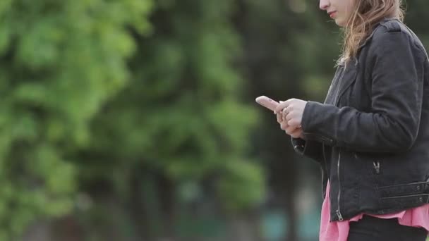 Chica de chaqueta negra camina por la calle mirando su teléfono móvil . Imágenes de stock libres de derechos
