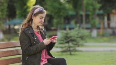 Parktaki bankta oturmuş cep telefonuyla konuşan esmer bir kız..