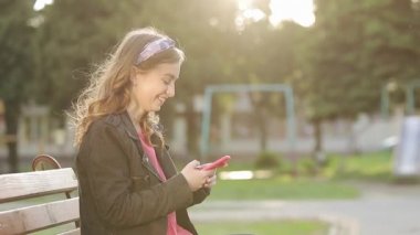 Güneş ışığındaki genç kızın elindeki akıllı telefon aygıtı ekranda tıklayıp mesajlaşırken. Açık hava..