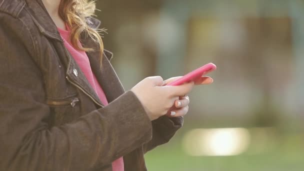 Tett inntil smarttelefonen i hendene på den unge jenta i sollys mens hun banker og tekster på er skjermen. Utendørs. – stockvideo