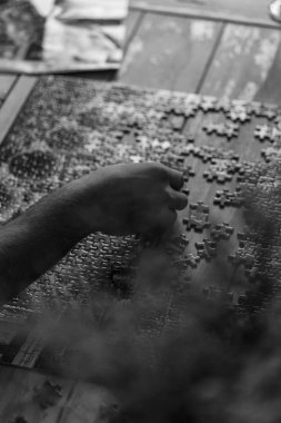 Siyah beyaz görüntü. Adam tahta sehpa üzerinde yapboz yapıyor. Siyah beyaz görüntü.