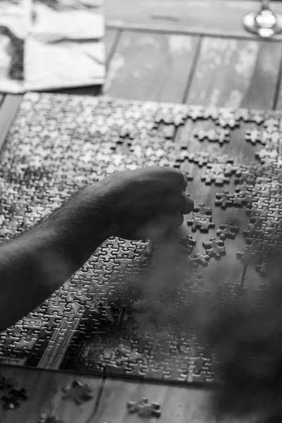 Imagen en blanco y negro. El hombre está haciendo rompecabezas en la mesa de centro de madera. Imagen en blanco y negro —  Fotos de Stock