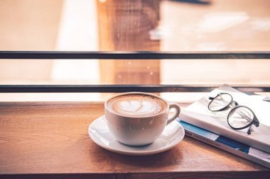 Kahvehanenin büyük penceresi önünde ahşap masada beyaz kahve fincan latte kahve.