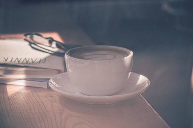 Kahvehanenin büyük penceresi önünde ahşap masada beyaz kahve fincan latte kahve.