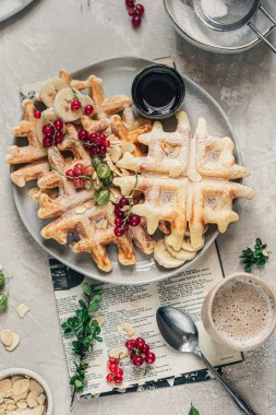 Kırmızı üzümlü çıtır Belçika waffleları, bektaşi üzümü, akçaağaç şurubu ve gri seramik tabakta pudra şekeri.