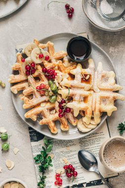 Kırmızı üzümlü çıtır Belçika waffleları, bektaşi üzümü, akçaağaç şurubu ve gri seramik tabakta pudra şekeri.