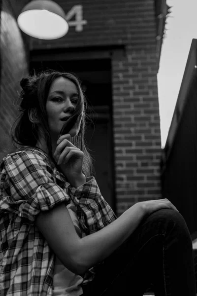 Mujer con el pelo largo en la calle. Retrato en blanco y negro. Muro de ladrillo detrás del modelo. Traje de moda estilo callejero. Traje de estilo de vida urbano. Camisa a cuadros, camiseta blanca. Chica rebelde. Diferentes emociones . —  Fotos de Stock