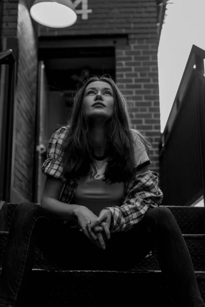 Mujer con el pelo largo en la calle. Retrato en blanco y negro. Muro de ladrillo detrás del modelo. Traje de moda estilo callejero. Traje de estilo de vida urbano. Camisa a cuadros, camiseta blanca. Chica rebelde. Diferentes emociones . —  Fotos de Stock