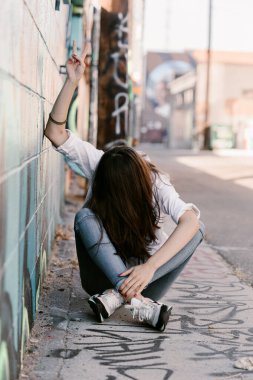 Beyaz gömlekli güzel bir kız, kırmızı dudaklı mavi kot pantolon. Sokakta poz vermek. Yerde oturuyordum. Uzun saçlı. Sakız. Güneşli bir gün. Sanat Bölgesi. Sıska kız modelliği. Güzel kadın, moda kızı.