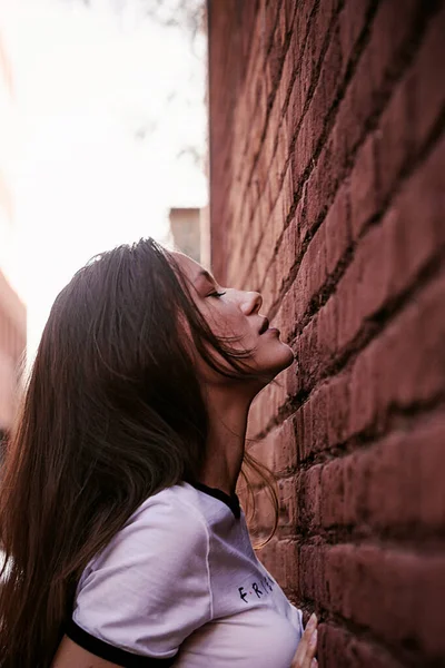 Mujer con el pelo largo en la calle. Pared de ladrillo rojo detrás del modelo. Traje de moda estilo callejero. Traje de estilo de vida urbano. Camisa a cuadros, camiseta blanca. Chica rebelde. Mostrando diferentes emociones. Sexy labios rojos . —  Fotos de Stock