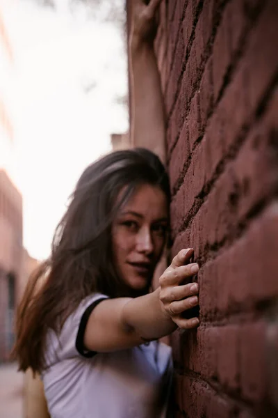 Mujer con el pelo largo en la calle. Pared de ladrillo rojo detrás del modelo. Traje de moda estilo callejero. Traje de estilo de vida urbano. Camisa a cuadros, camiseta blanca. Chica rebelde. Mostrando diferentes emociones. Sexy labios rojos . —  Fotos de Stock