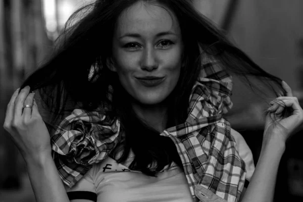 Mujer con el pelo largo en la calle. Retrato en blanco y negro. Muro de ladrillo detrás del modelo. Traje de moda estilo callejero. Traje de estilo de vida urbano. Camisa a cuadros, camiseta blanca. Chica rebelde. Diferentes emociones . —  Fotos de Stock