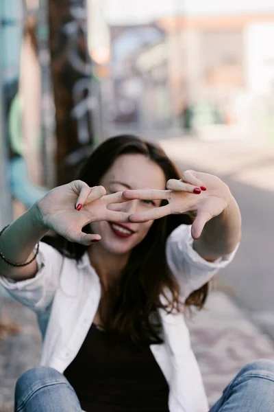 Pretty girl in white shirt, blue jeans with red lips. Posing in street. Sitting on the floor. Long hair. Bubble gum. Sunny day. Art district. Skinny girl modeling. Pretty woman, fashion girl.