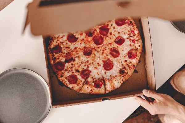 Food delivery. Ordering dinner online from the restaurant. New York style pizza and movie night. Family meal at home. Pepperoni and cheese topping. Cardboard box. Friday party. Comfort food.