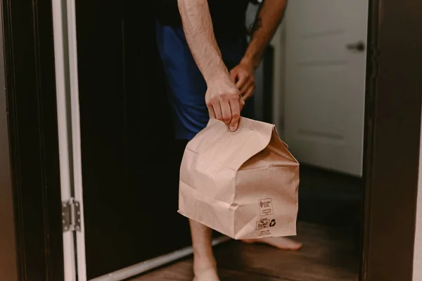 Contactless food delivery from restaurant. New normal. Coronavirus covid-19 reality. Order dinner online. No dining in. Quarantine life. Recycle paper bag. Chinese meal. Man holds bag apartment door.