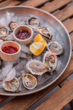 Kırmızı sirkeli ve yaban turplu domates soslu istiridye tabağı. Deniz ürünleri tabağı. Okyanus yemeği. Çiğ deniz ürünleri. Limon dilimleri. Taze ve besleyici bir yemek. Lüks yemek. Güzel bir akşam yemeği..