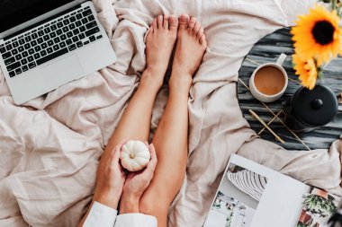 Kadın yatakta kahvenin tadını çıkarıyor. Laptop üzerinde çalışıyorum. Ayçiçeği aranjmanı. Yatak odası titreşimi. Sonbahar sezonu. Evimde gibi hissediyorum. Küçük şeylerden zevk alıyorum. Sonbahar renkleri ve havası. Evde çalış..