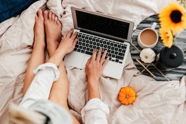 Kadın yatakta kahvenin tadını çıkarıyor. Laptop üzerinde çalışıyorum. Ayçiçeği aranjmanı. Yatak odası titreşimi. Sonbahar sezonu. Evimde gibi hissediyorum. Küçük şeylerden zevk alıyorum. Sonbahar renkleri ve havası. Evde çalış..