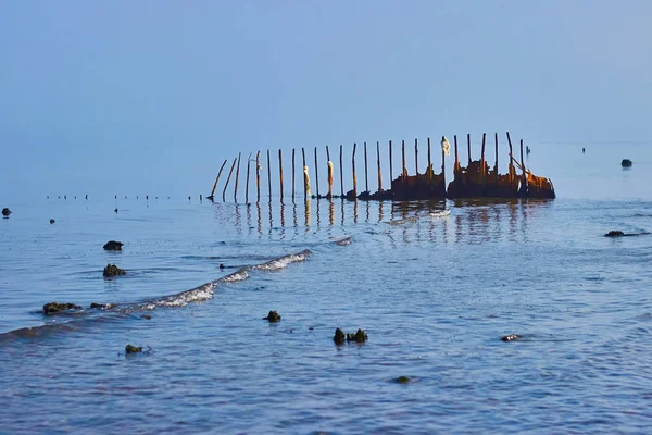 Old rusty breakwaters with ragged scraps of rope. Against the background of the sea merging with the sky. — Stock Photo, Image
