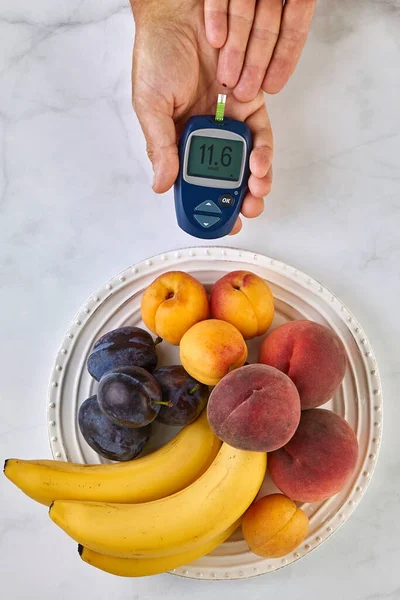 Un glucómetro en las manos de un hombre y un plato de fruta —  Fotos de Stock