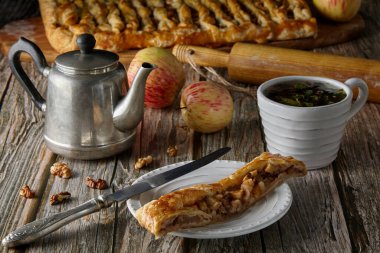 Elma, elma ve fındıklı lezzetli ev yapımı turta parçaları elmalı ve fındıklı bir fındıklı, klasik bir çaydanlık, bir fincan bitki çayı ve eski ahşap bir masanın üzerinde merdane.