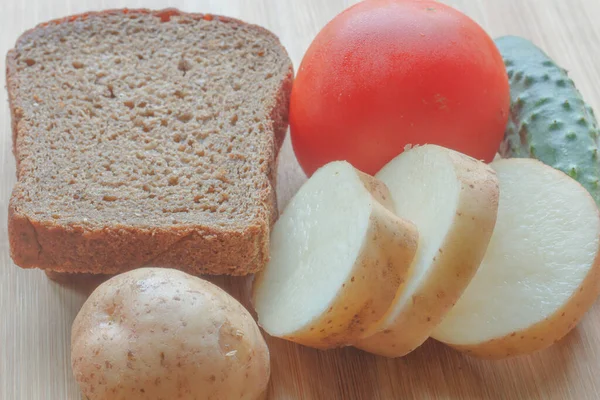  kahverengi ekmek, taze doğranmış patates, domates ve salatalık tahtada
