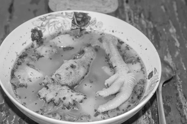 Moldavian borscht with a rooster\'s head and a cock\'s paw close-up on a table in black and white