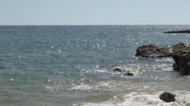 Kayaların üzerinde dalgalar, güneş su üzerinde parlar.