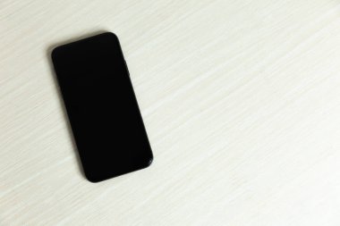 Beyaz masadaki kopyalama alanı olan siyah akıllı telefon.