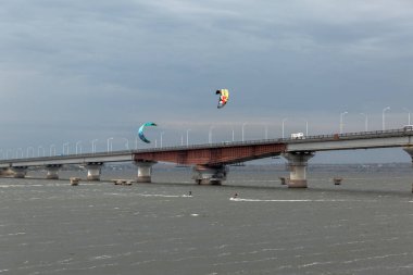  view from the pear on kitesurfers near bridge in the cloudy weather clipart