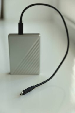 Arkaplanda penceresi olan beyaz masadaki siyah usb kablosu ile taşınabilir HDD