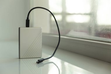 Arkaplanda penceresi olan beyaz masadaki siyah usb kablosu ile taşınabilir HDD
