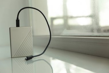 Arkaplanda penceresi olan beyaz masadaki siyah usb kablosu ile taşınabilir HDD