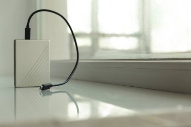 Arkaplanda penceresi olan beyaz masadaki siyah usb kablosu ile taşınabilir HDD