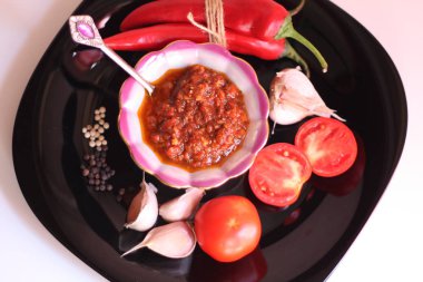 Adjika domates sosu ve siyah bir tabak üzerinde malzemeler