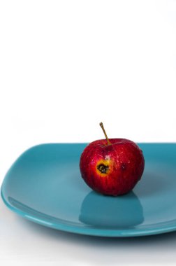 Beyaz arka planda, turkuaz bir plaka üzerinde çürük kırmızı elma. 