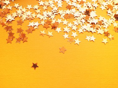 Altın yıldızlar turuncu kağıt arka planda parlıyor