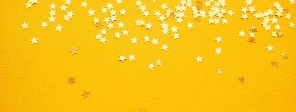 Złote gwiazdki błyszczą na żółtym tle papieru — Zdjęcie stockowe