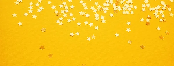 Estrelas douradas brilham sobre fundo de papel amarelo — Fotografia de Stock