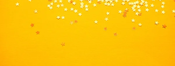 Złote gwiazdki błyszczą na żółtym tle papieru — Zdjęcie stockowe