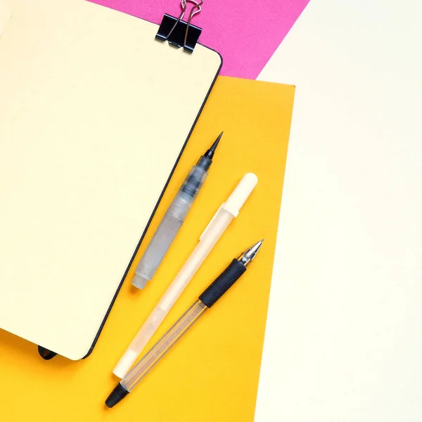 Modello con taccuino bianco e strumenti di disegno su sfondo bianco, giallo e rosa . — Foto Stock