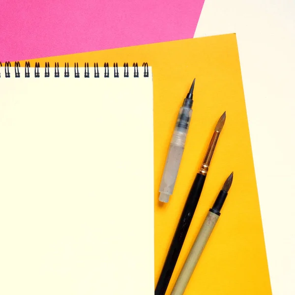 Modèle avec carnet vierge et outils de dessin sur fond papier blanc, jaune et rose . — Photo