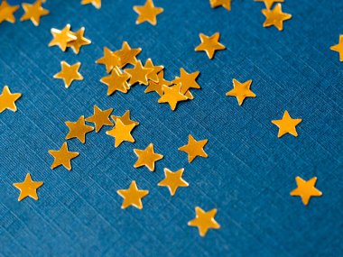 Altın yıldızlı simli konfeti mavi kağıdın üzerine sıçradı. Neşeli pırıltılı parıltı arkaplanı.