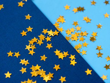 Altın yıldızlı simli konfeti mavi kağıdın üzerine sıçradı. Neşeli pırıltılı parıltı arkaplanı.