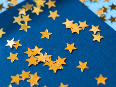 Altın yıldızlı simli konfeti mavi kağıdın üzerine sıçradı. Neşeli pırıltılı parıltı arkaplanı.