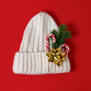 Baston şekerle süslenmiş yün örülmüş sıcak bir şapka, her zaman yeşil olan bir dal ve turkuaz renkli bir arka planda altın bir fiyonk. Şenlikli Noel kıyafetleri arka planında.