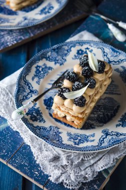 french pastry with custard and blackberries in blue plate on wooden table clipart